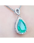 Teardrop-shaped emerald pendant on a chain against a light skin background.