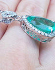 Emerald green gemstone pendant on a gold chain held between fingers.