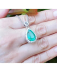 5.83 ct. Colombian emerald pear cut pendant with diamond halo on 18K white gold chain, held in hand.