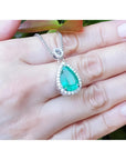 5.83 ct. Colombian emerald pear cut pendant with diamond halo on 18K white gold chain, held in hand.