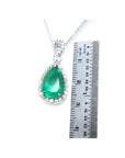 Pear-cut Colombian emerald pendant with diamond halo in 18K white gold, next to a ruler.