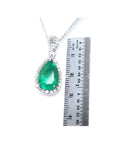 Pear-cut Colombian emerald pendant with diamond halo in 18K white gold, next to a ruler.