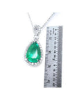 Pear-cut Colombian emerald pendant with diamond halo in 18K white gold, next to a ruler.