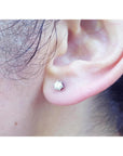 A woman's ear wearing a 14k white gold diamond stud earring crew backs.