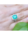 Emerald-cut natural Colombian emerald ring with diamond halo, set in 14k white gold on a hand.