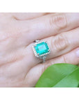 Emerald-cut natural Colombian emerald ring with diamond halo, set in 14k white gold on a hand.