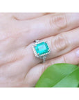 Emerald-cut natural Colombian emerald ring with diamond halo, set in 14k white gold on a hand.