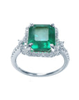 An emerald-cut emerald engagement ring with a halo diamond in white gold on a white background.