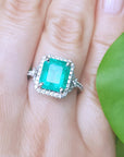 A brides' emerald engagement ring on a finger with a green leaf background.