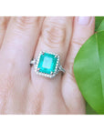 A brides' emerald engagement ring on a finger with a green leaf background.