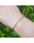 Bracelet with emerald gemstones on a wrist against a green leafy background