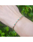 Flexible 14K yellow gold bangle bracelet with genuine Colombian emeralds and accent diamonds on a wrist.