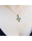 18K yellow gold cross pendant with four round Colombian emeralds and a small diamond, worn on a gold chain.