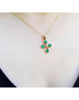 18K yellow gold cross pendant with four round Colombian emeralds and a small diamond, worn on a gold chain.