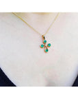 18K yellow gold cross pendant with four round Colombian emeralds and a small diamond, worn on a gold chain.