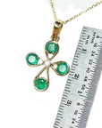 Gold necklace with a four-leaf clover pendant featuring natural emeralds and a ruler for scale on a white background.
