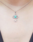 A white gold necklace with a round cut emerald pendant on a person wearing a black top.