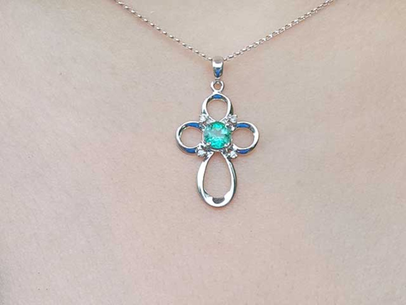 White gold necklace with a clover-shaped cross pendant featuring a green gemstone on a person's neck
