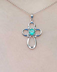 White gold necklace with a clover-shaped cross pendant featuring a green gemstone on a person's neck