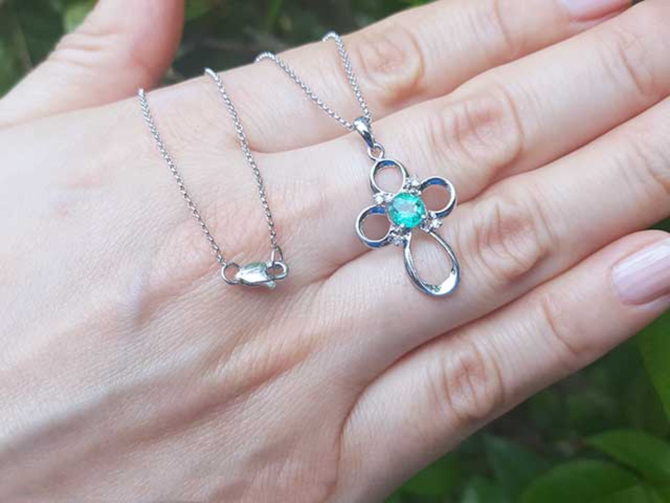 14k white gold necklace with a clover-shaped pendant featuring a round cut emerald on a hand.