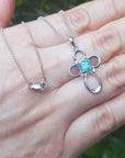 14k white gold necklace with a clover-shaped pendant featuring a round cut emerald on a hand.