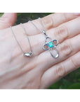 14K white gold cross pendant with a round-cut Colombian emerald and diamond accents, on a delicate chain.