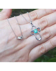 14K white gold cross pendant with a round-cut Colombian emerald and diamond accents, on a delicate chain.