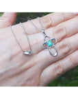 14K white gold cross pendant with a round-cut Colombian emerald and diamond accents, on a delicate chain.