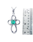 14K white gold cross pendant with a round green Colombian emerald and diamond accents, next to a ruler.