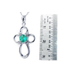 14K white gold cross pendant with a round green Colombian emerald and diamond accents, next to a ruler.