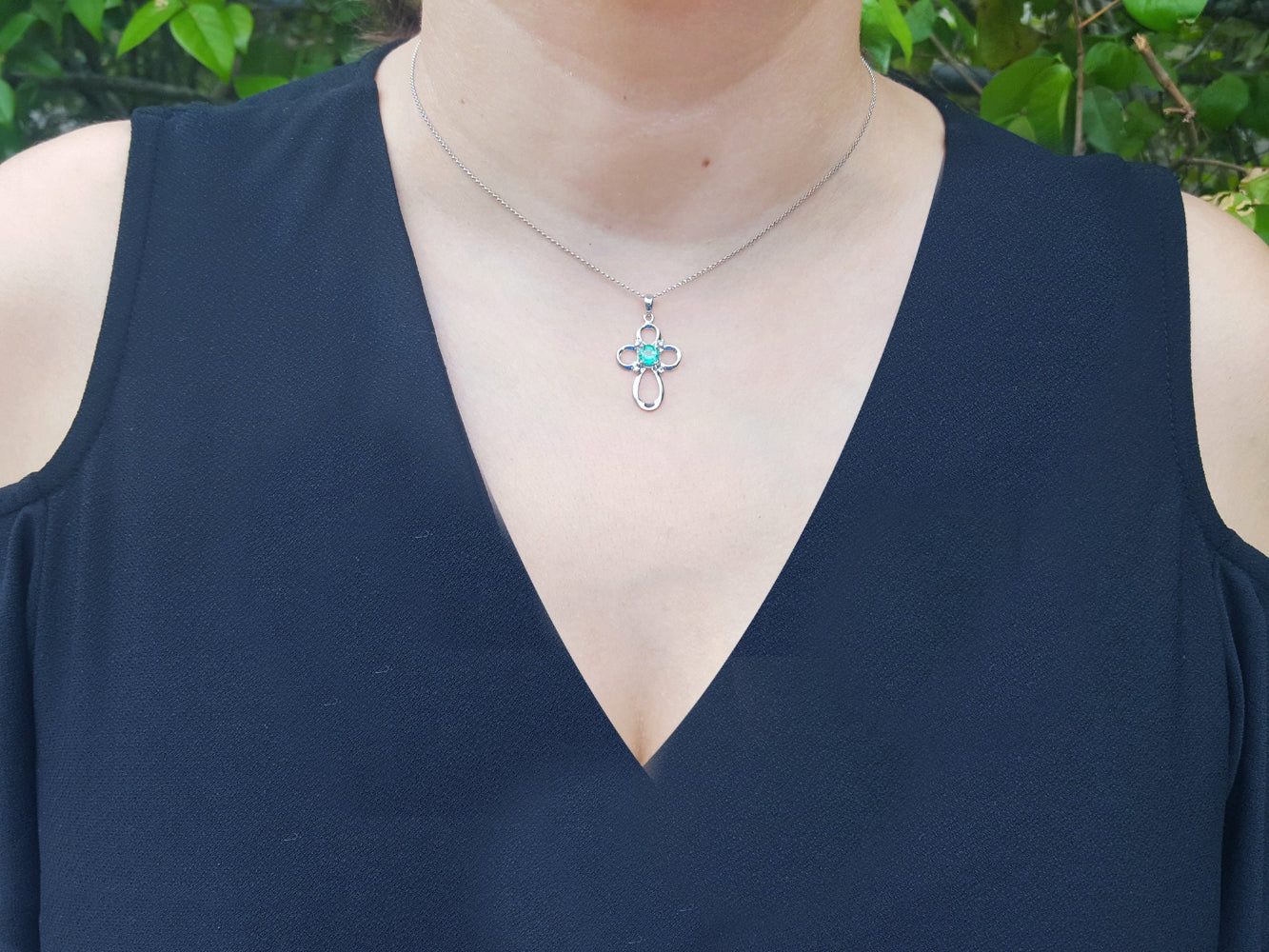 A woman wearing a black sleeveless top with a necklace featuring an emerald cross pendant.