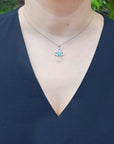 A woman wearing a black sleeveless top with a necklace featuring an emerald cross pendant.
