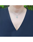 14K white gold cross pendant with a 0.57 ct round Colombian emerald and diamond accents, worn on a necklace.