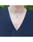 14K white gold cross pendant with a 0.57 ct round Colombian emerald and diamond accents, worn on a necklace.