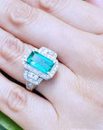 Emerald ring with diamond accents on a hand