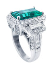 Elegant emerald ring with a halo diamond and diamond accents on a white background