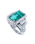 18K white gold ring with a vibrant emerald-cut Colombian emerald, haloed by diamonds and baguette side stones.