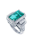 18K white gold ring with a vibrant emerald-cut Colombian emerald, haloed by diamonds and baguette side stones.