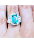 A GIA certified genuine Colombian emerald ring rectangular emerald-cut surrounded by natural diamonds in 18k white gold on a finger.