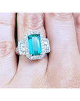 A GIA certified genuine Colombian emerald ring rectangular emerald-cut surrounded by natural diamonds in 18k white gold on a finger.