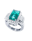 18K white gold ring with a vibrant emerald-cut Colombian emerald, haloed by diamonds and baguette side stones.