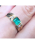 A yellow gold men's ring with a bezel set emerald on a person's finger