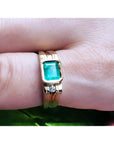 Men's 14K yellow gold ring with a bezel-set emerald and side diamond accents on a finger.
