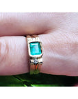 Men's 14K yellow gold ring with a bezel-set emerald and side diamond accents on a finger.