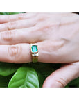 Men's 14K yellow gold ring with a rectangular natural emerald and two side diamonds, worn on a hand.