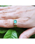 Men's 14K yellow gold ring with a rectangular natural emerald and two side diamonds, worn on a hand.