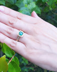 Hand wearing a Mother's Day gift emerald ring against a green leafy background.