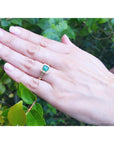 Hand wearing a Mother's Day gift emerald ring against a green leafy background.