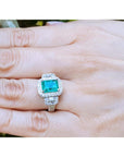 Emerald engagement ring with diamond accents on a hand.