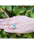 Hand wearing an 18K white gold engagement ring with a vibrant emerald and diamond halo.